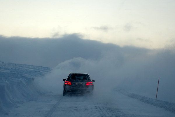 Vor dem MB steckt der Schneepflug in seiner selbstproduzierten Wolke. Links sieht man, wie hoch der Schnee ohne Pflug auf der Straße wäre.